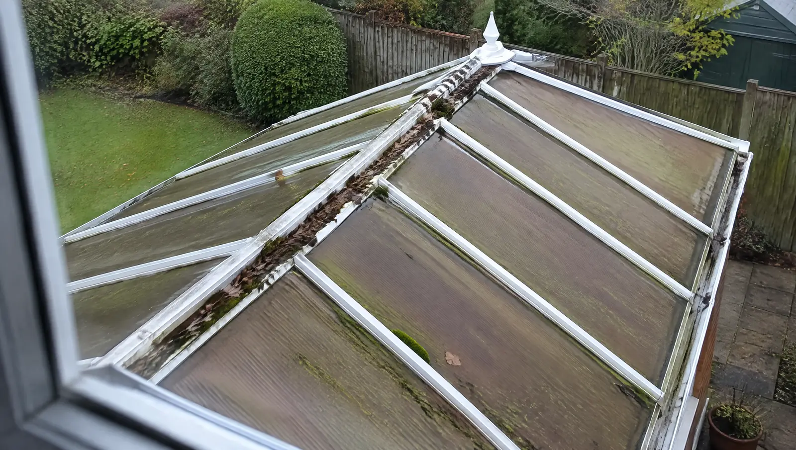 Ageing brown polycarbonate conservatory roof with algae streaks seen from an upstairs window