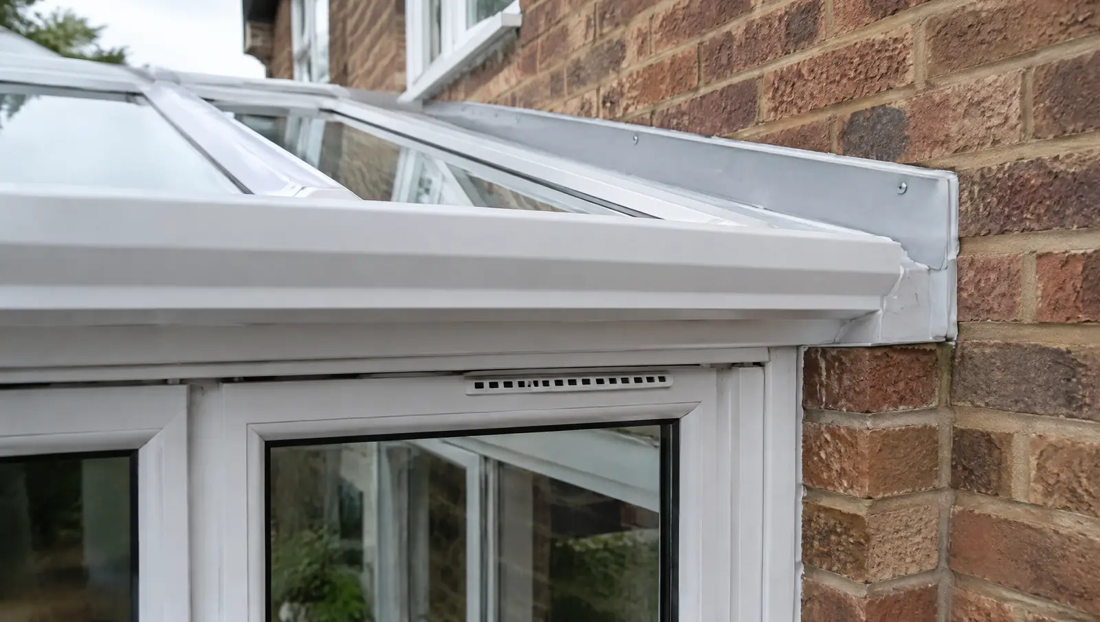 Close-up of a white uPVC conservatory frame meeting a brick dwarf wall and the wall plate