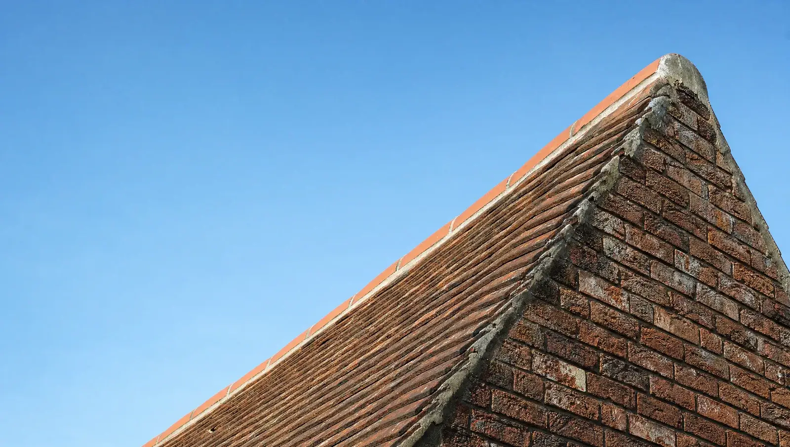 Looking up a steep clay-tiled roof slope against a blue sky, showing the angle of the pitch