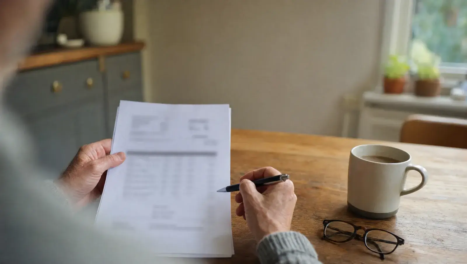 Hands reviewing a printed itemised roofing quotation with a pen at a kitchen table