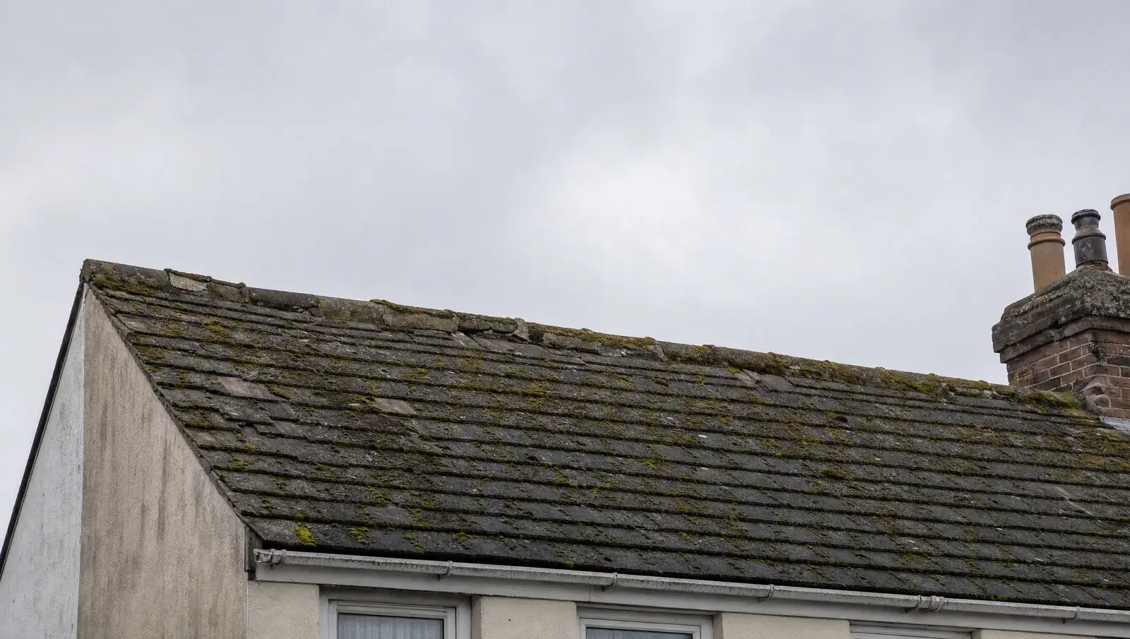 Tired UK terraced roof with slipped tiles, heavy moss and crumbling ridge mortar