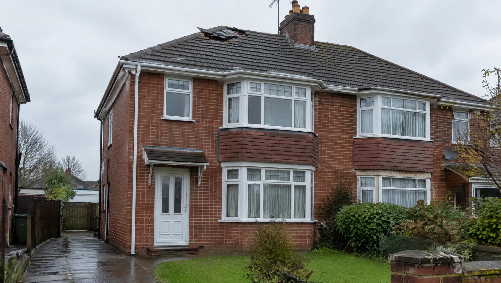 Red brick British semi-detached house seen from the front garden on an overcast day
