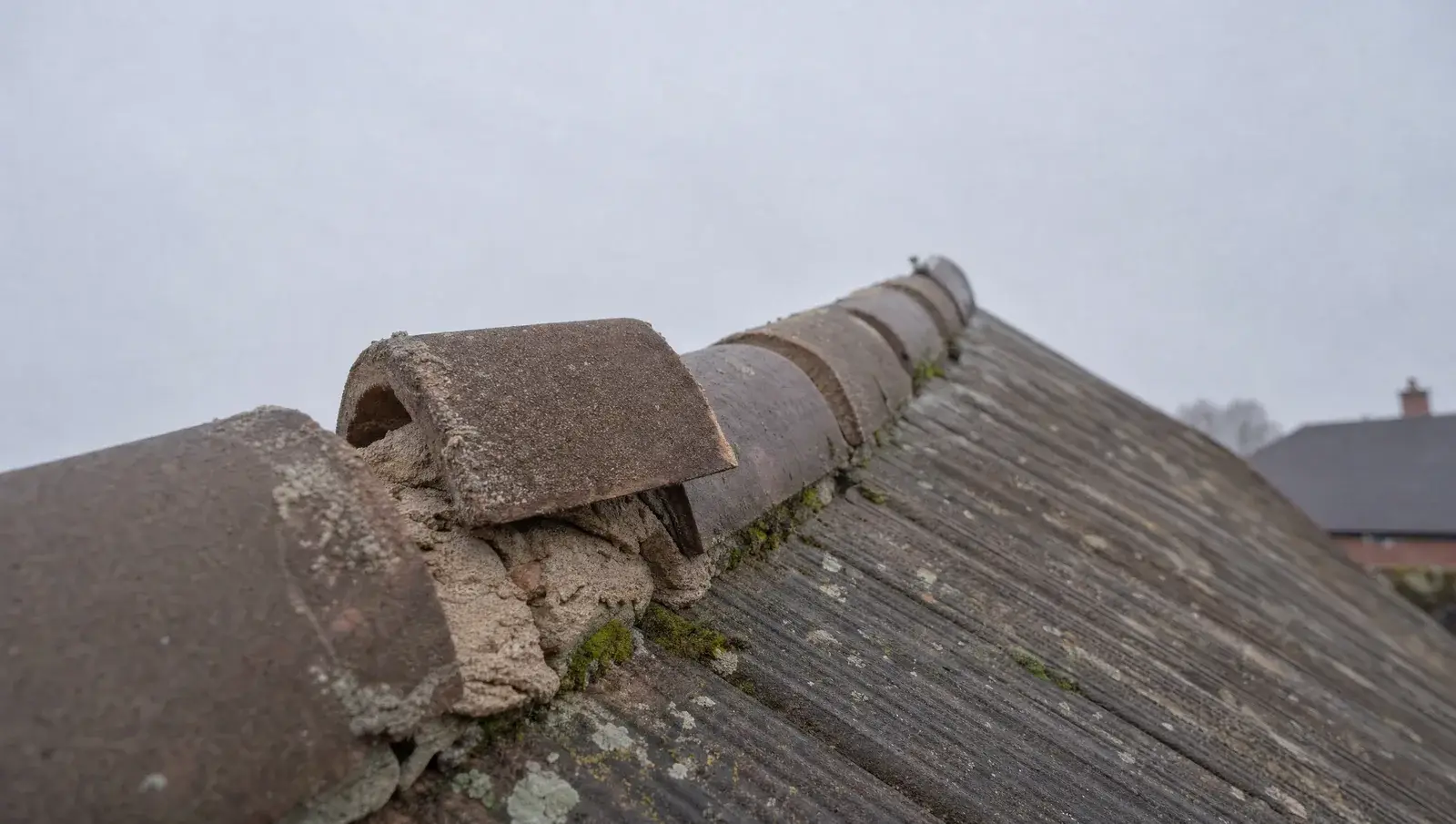 Roof ridge line with cracked bedding mortar and a displaced ridge tile on a UK house