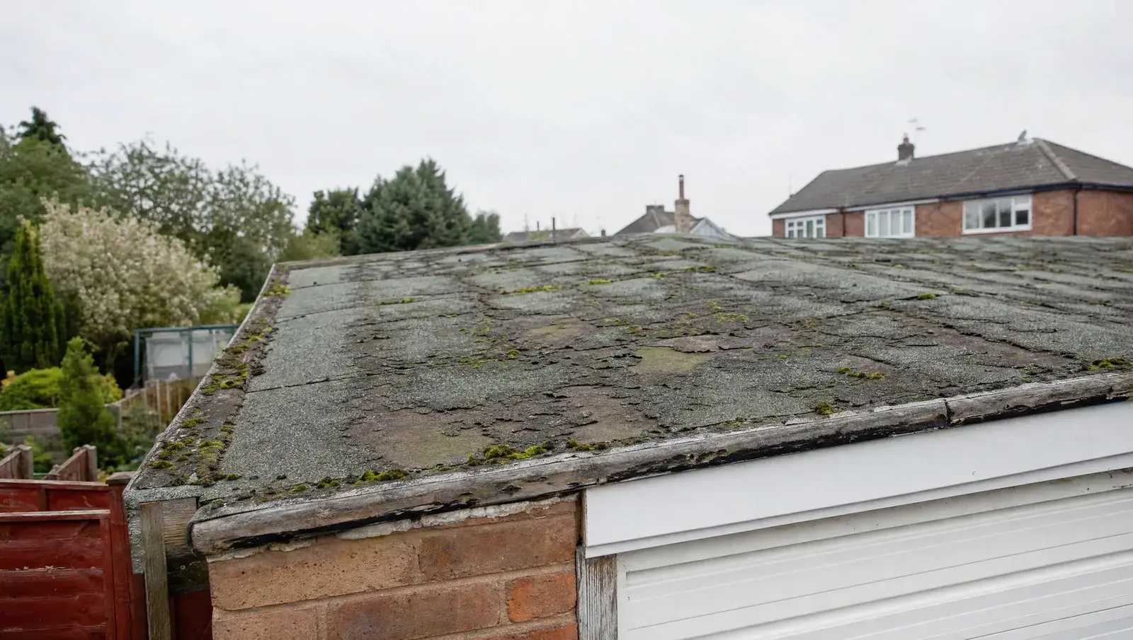 Aged felt garage roof with blisters, cracking and moss along the seams, viewed from a ladder