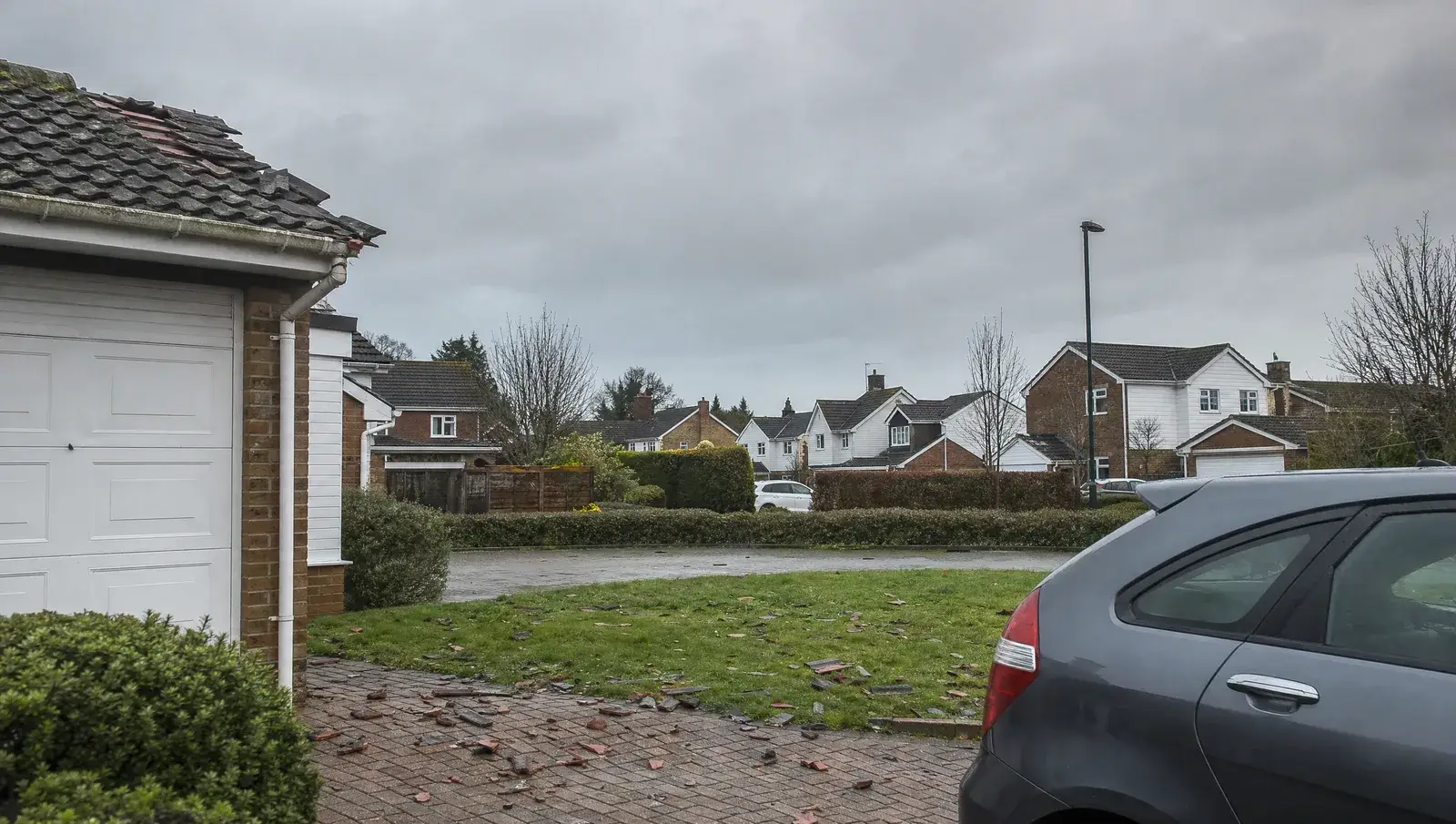 Broken roof tiles scattered across a UK driveway and lawn after a storm
