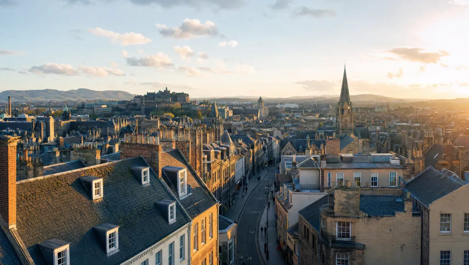 Elevated view across varied UK city rooftops at golden hour, slate and tile