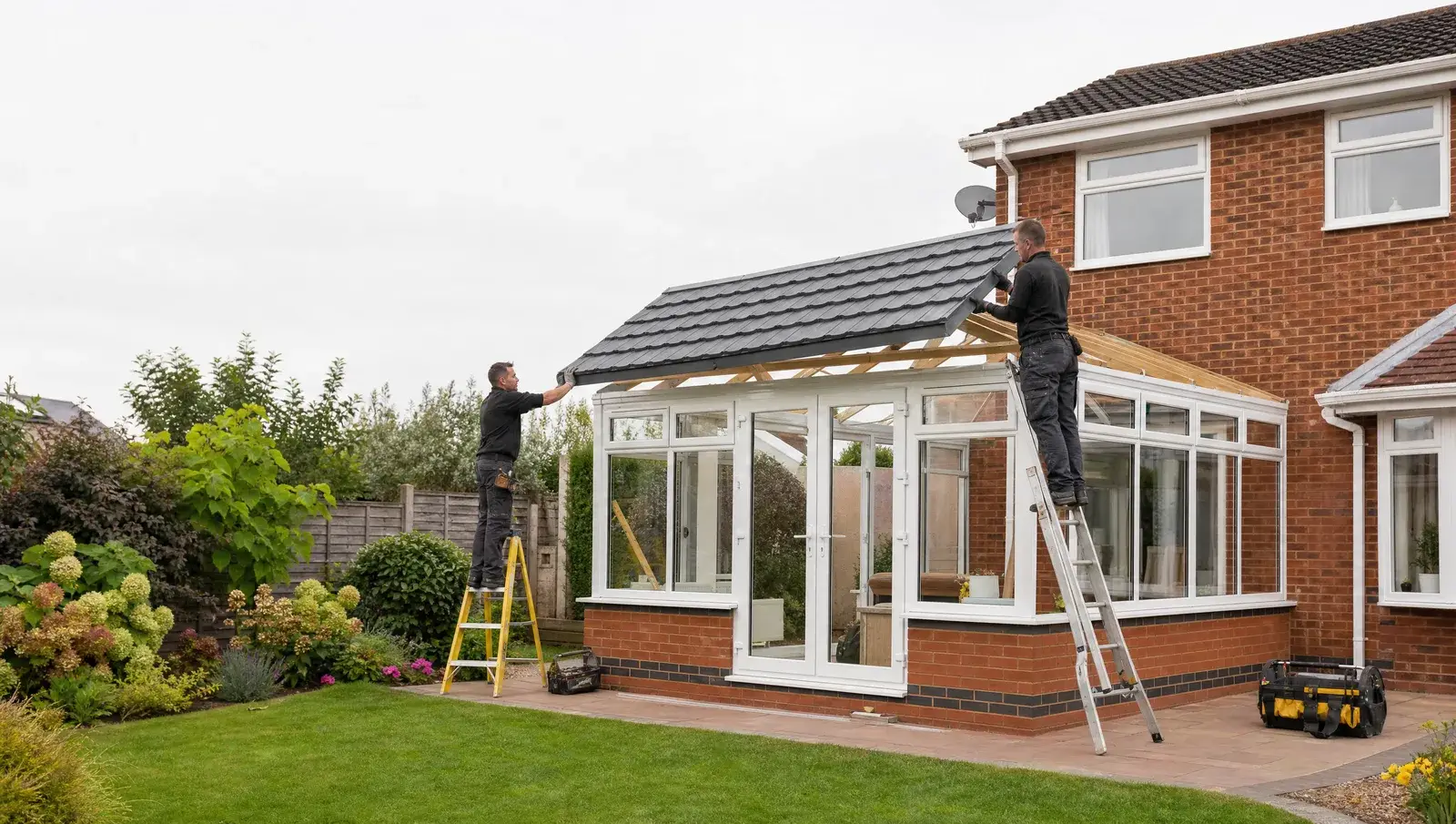 Installers lifting a lightweight tiled roof panel onto a conservatory frame in a garden
