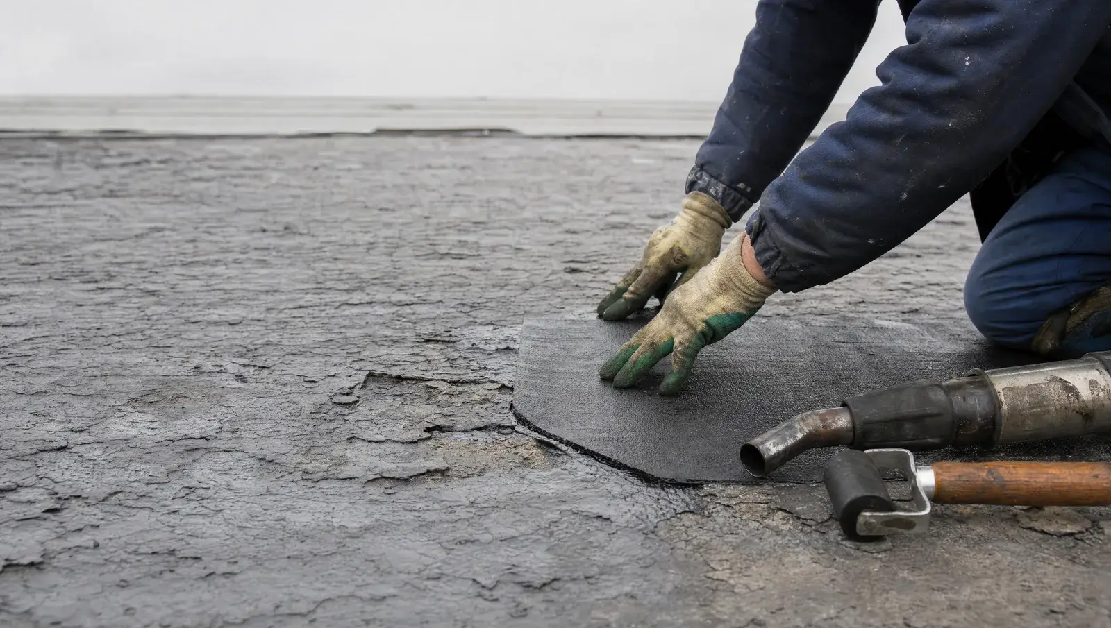 Close-up of a roofer applying a felt patch repair to a blistered flat roof