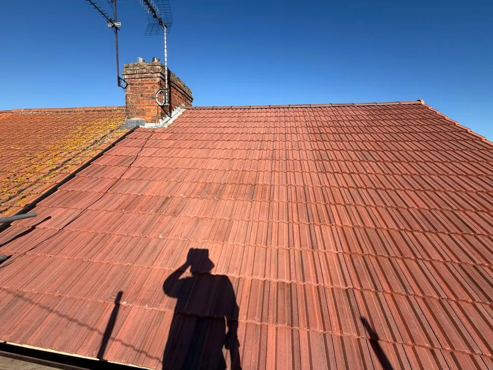 Finished red interlocking tile roof slope with a brick chimney under blue sky