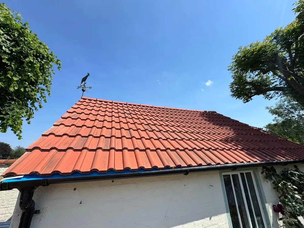 Finished red tile roof on a white single-storey building with a weathervane on the ridge