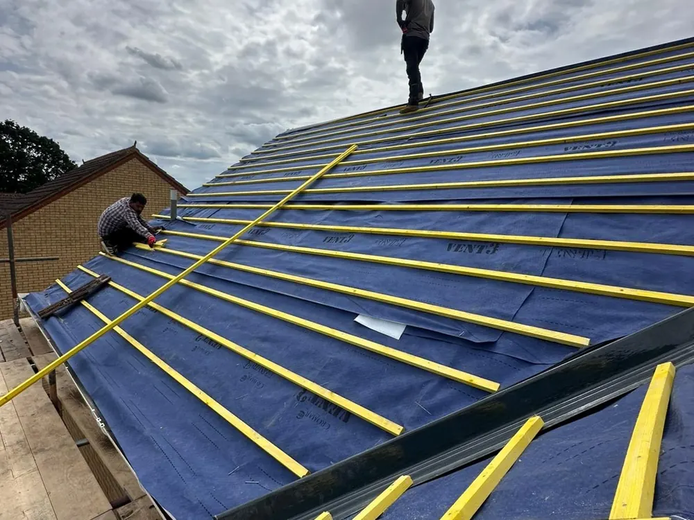 Pitched roof in new blue membrane with yellow graded battens, roofers at the ridge