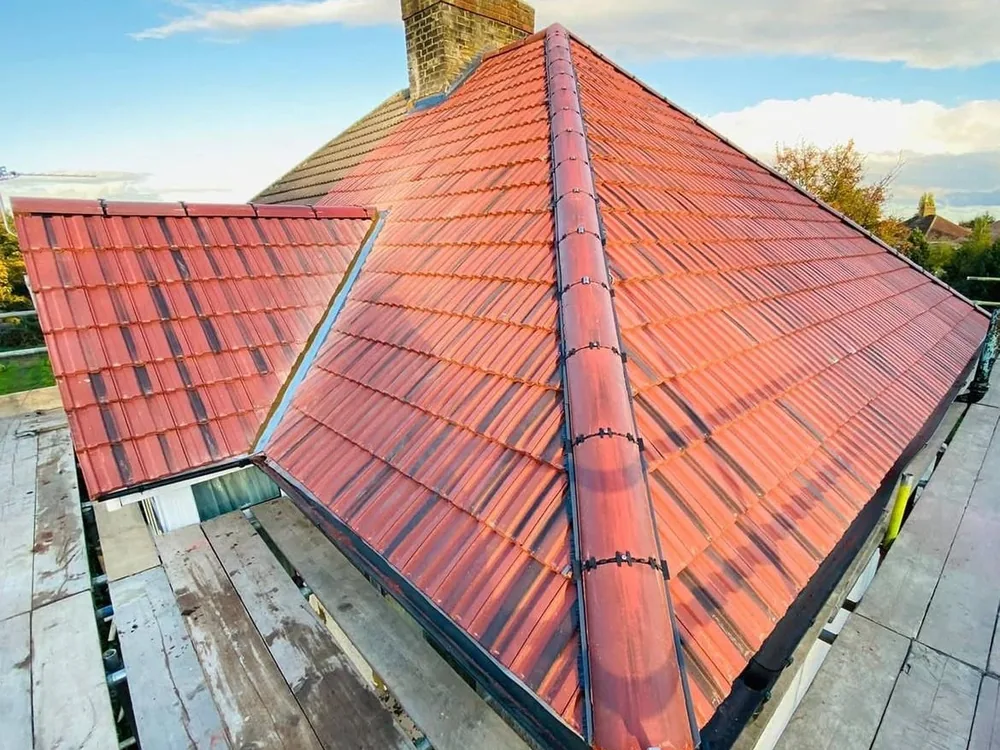 New red interlocking tile hip roof with a dry-fix ridge under blue sky