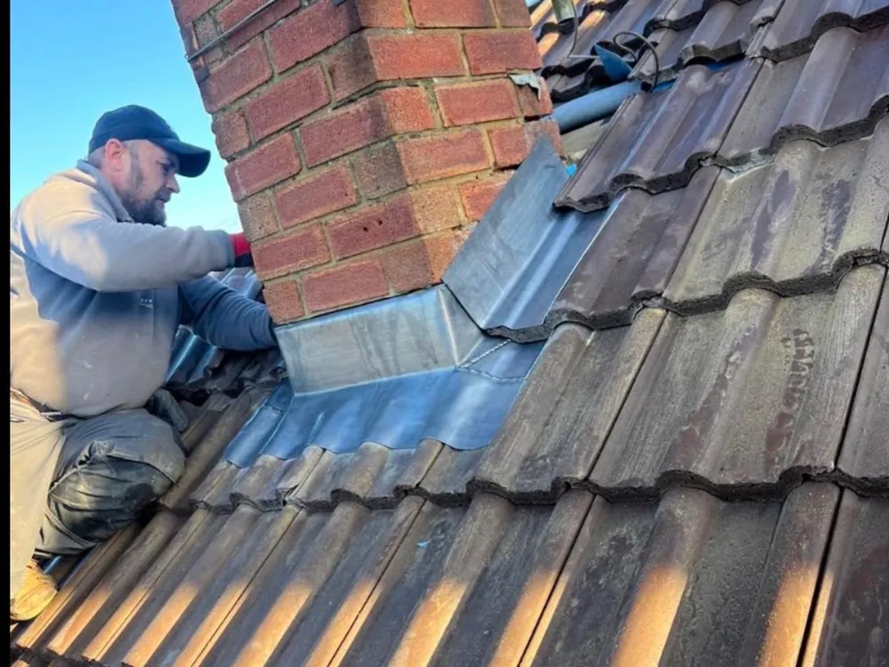 Roofer dressing new lead flashing around a brick chimney on a concrete tile roof