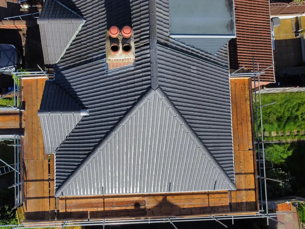 Aerial view of a new grey tiled roof built around a chimney, scaffold still up