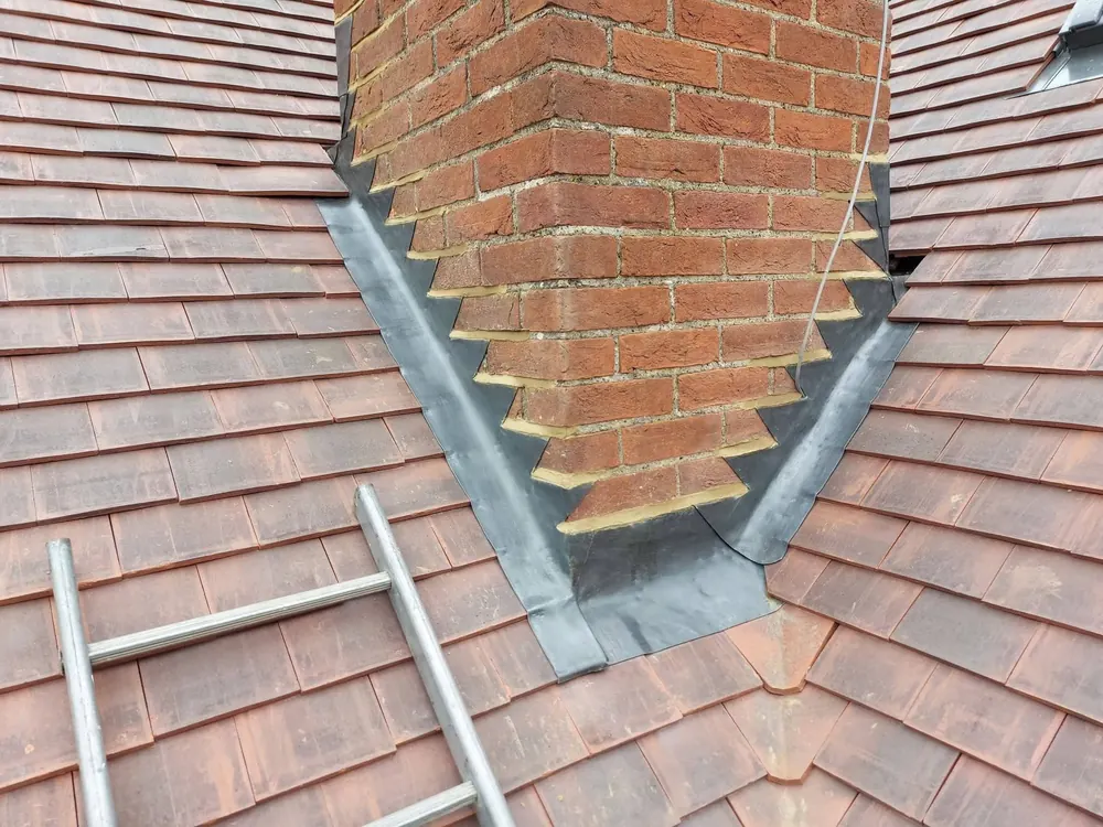 New lead flashing stepped around a brick chimney on a plain tile roof