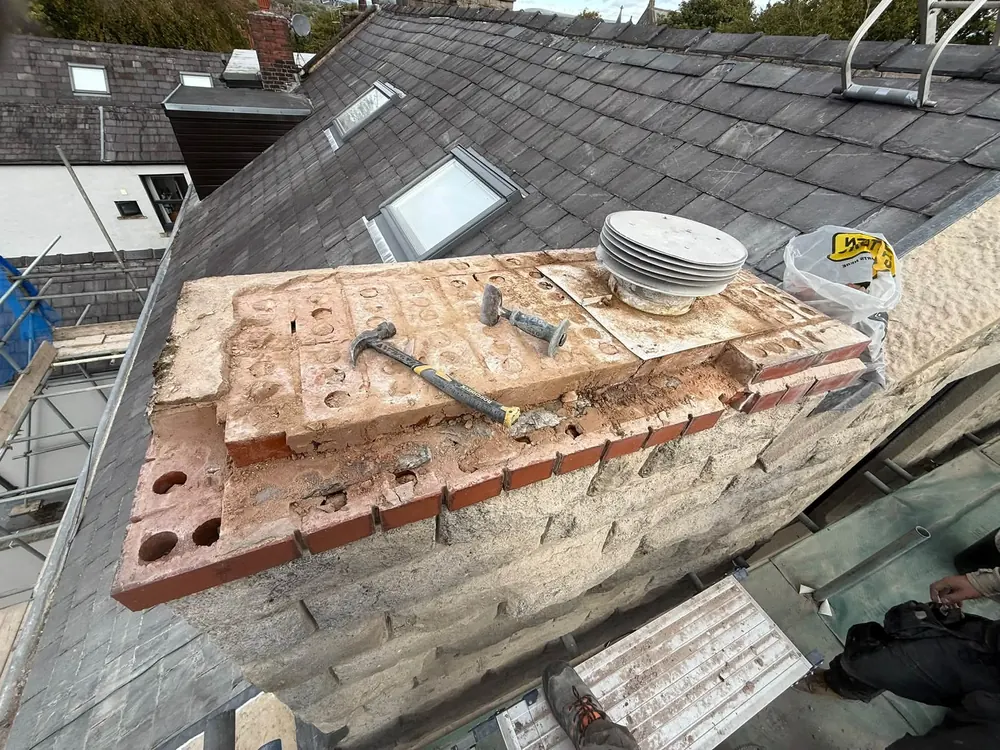Chimney stack being rebuilt from the scaffold on a slate roof