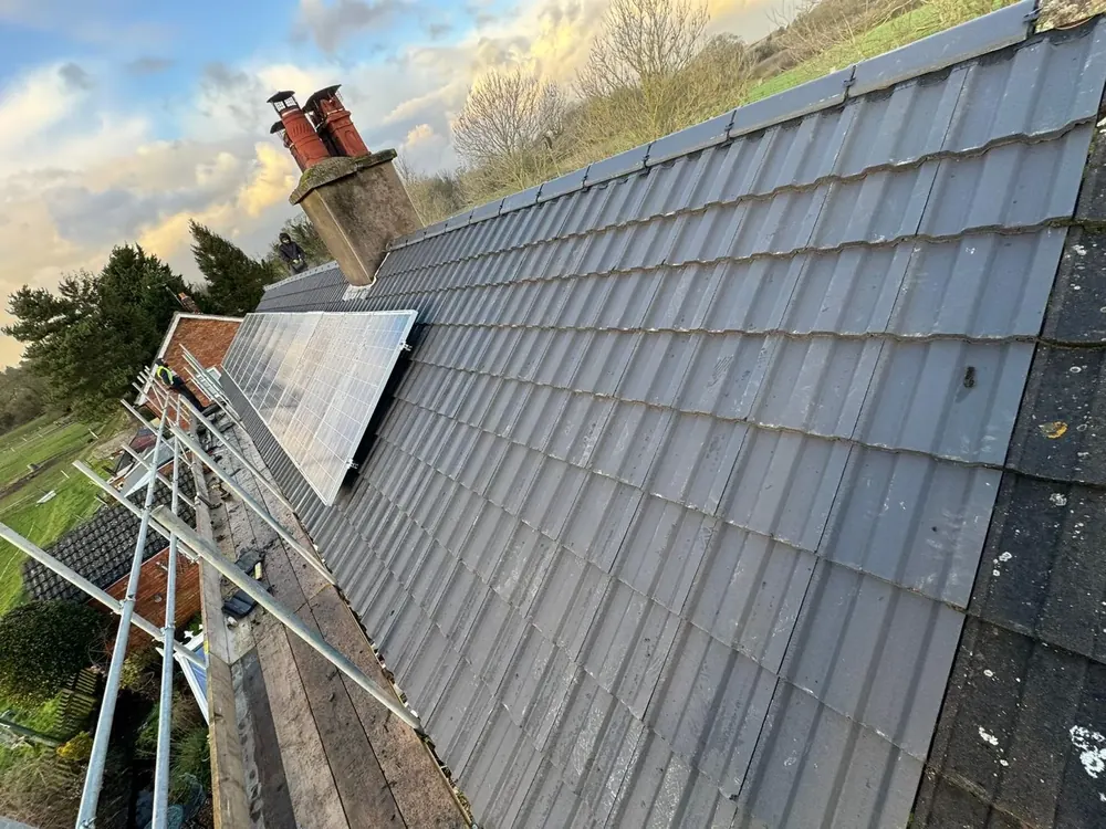 Grey tiled pitched roof with a chimney, solar panels and scaffolding