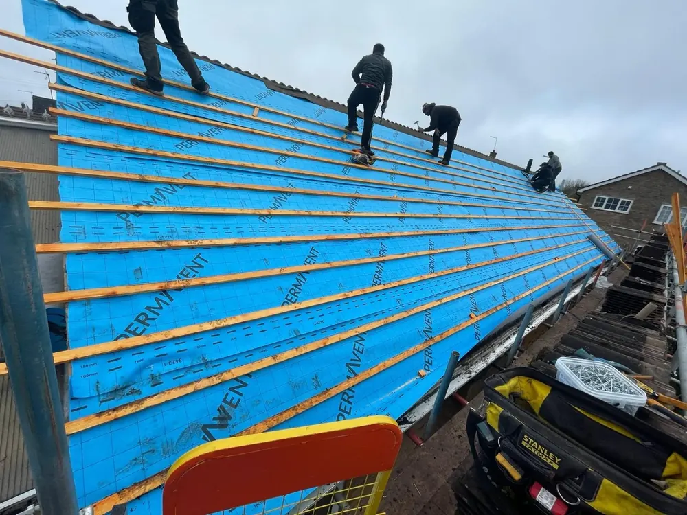 Roofers working on blue roofing membrane and timber battens