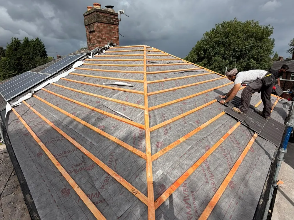 Roofer fixing new battens over breathable membrane on a hip roof re-roof