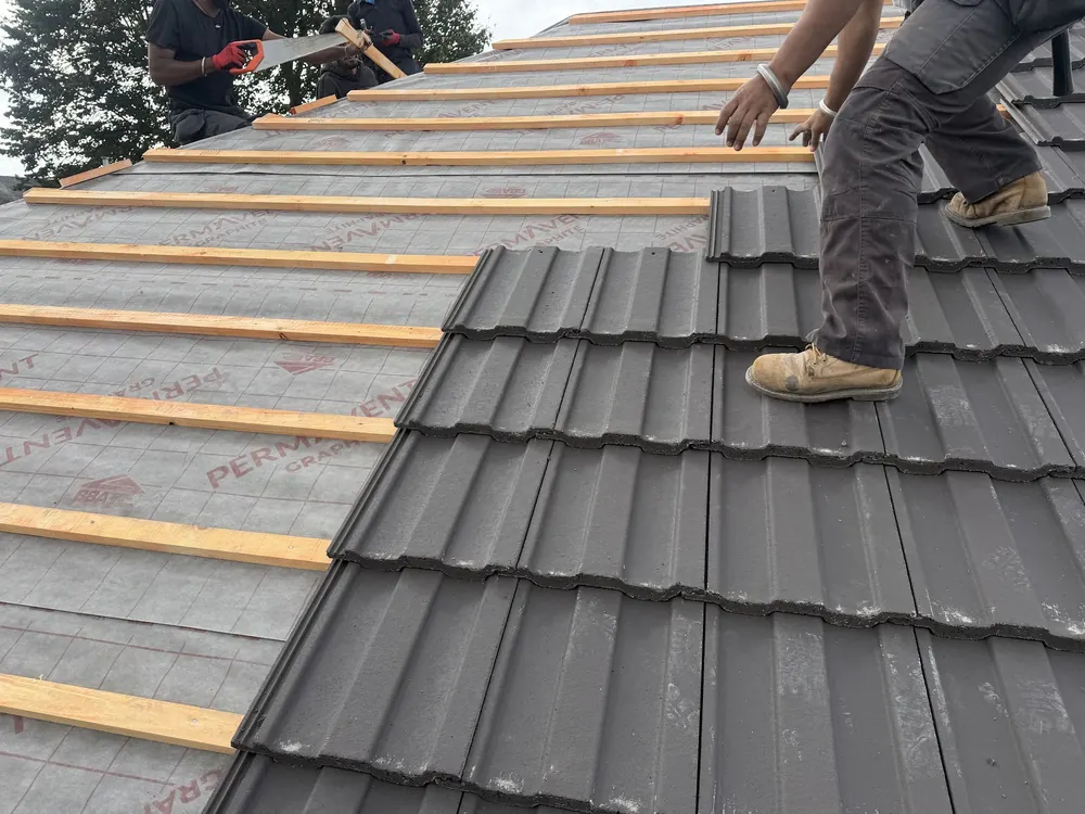 Roofer laying grey interlocking tiles over new battens