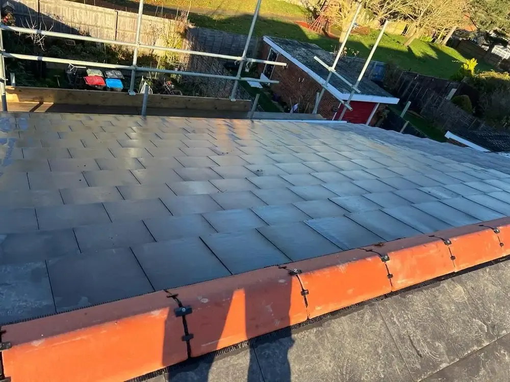 Finished slate-effect roof with terracotta ridge tiles, seen from the scaffold