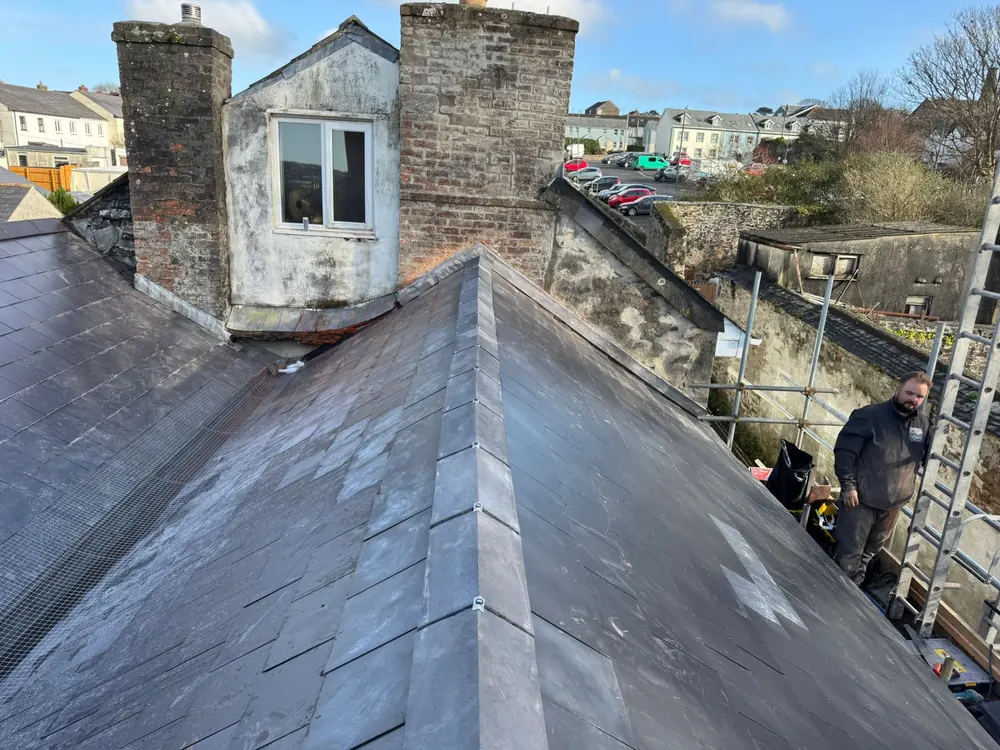 Finished slate roof with a new hip beside a dormer and two brick chimneys
