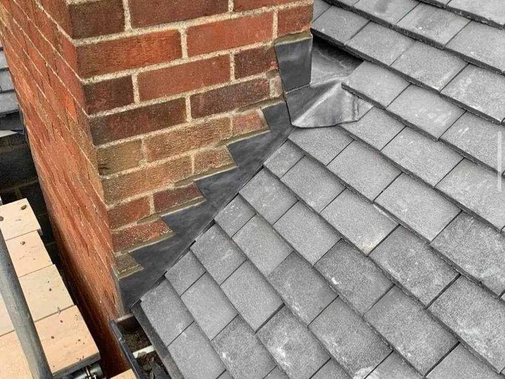 Lead soakers and flashing where grey tiles meet a brick chimney