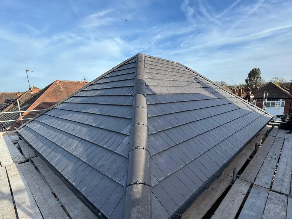 Grey slate-effect hip roof with ridge caps and scaffolding under a blue sky