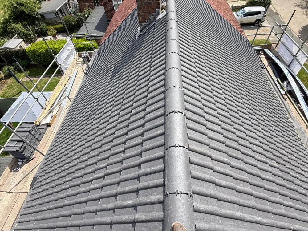 Completed grey tiled roof seen along the ridge towards a brick chimney