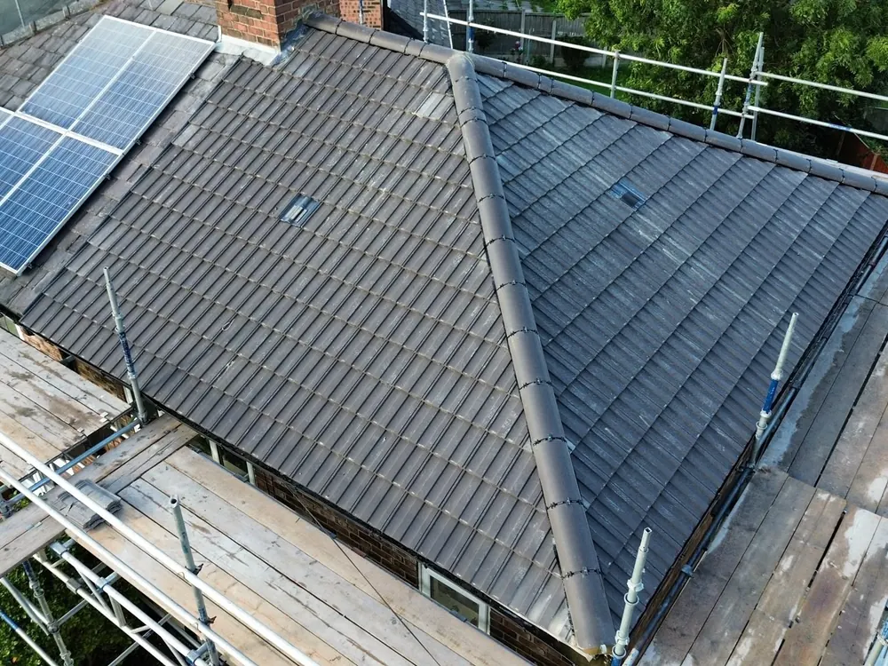 Grey tiled hip roof finished with solar panels beside it and scaffold round the edge