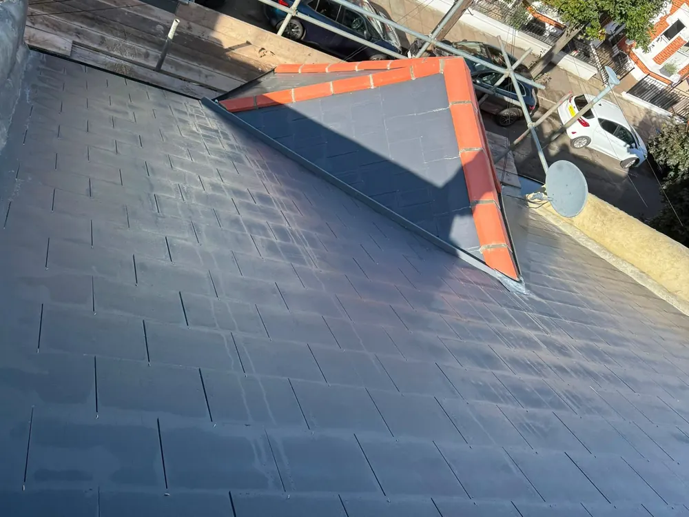 Slate roof with a new hip in red clay ridge tiles above the street