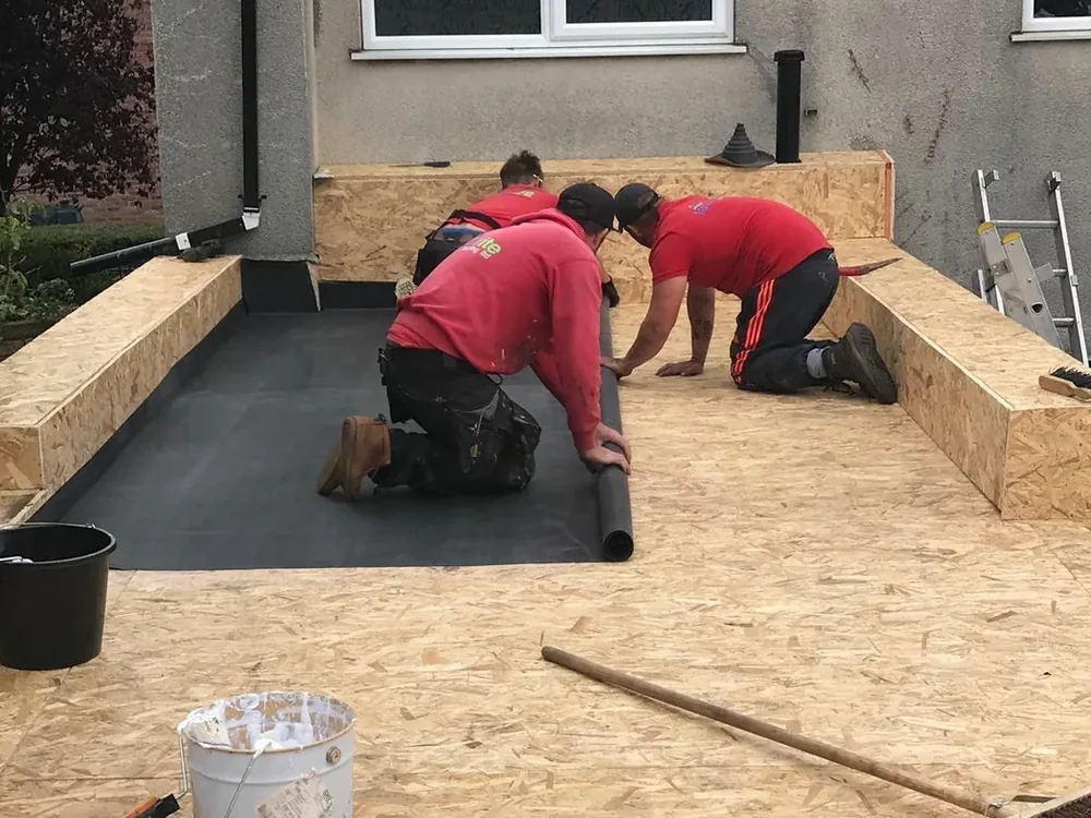 RoofRite roofers laying EPDM rubber membrane over a new deck on a rear extension