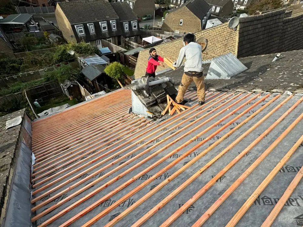 Re-roof in progress with new battens on membrane and two roofers cutting at the ridge