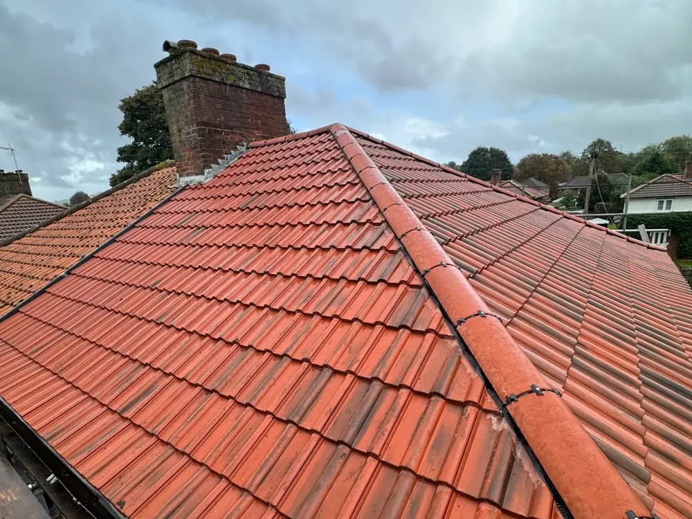 Red interlocking tiles on a hip roof with a brick chimney beyond