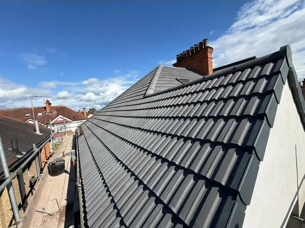 New dark grey interlocking tiles along a gable verge with a chimney at the far end
