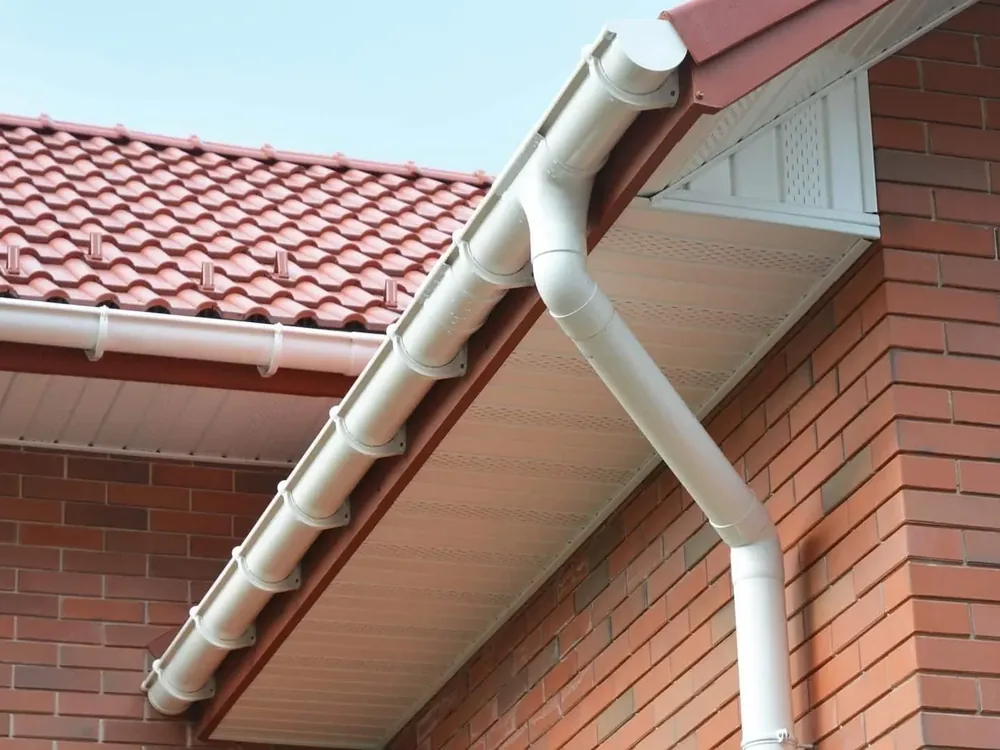 New white gutter, downpipe and soffit at a red brick house corner