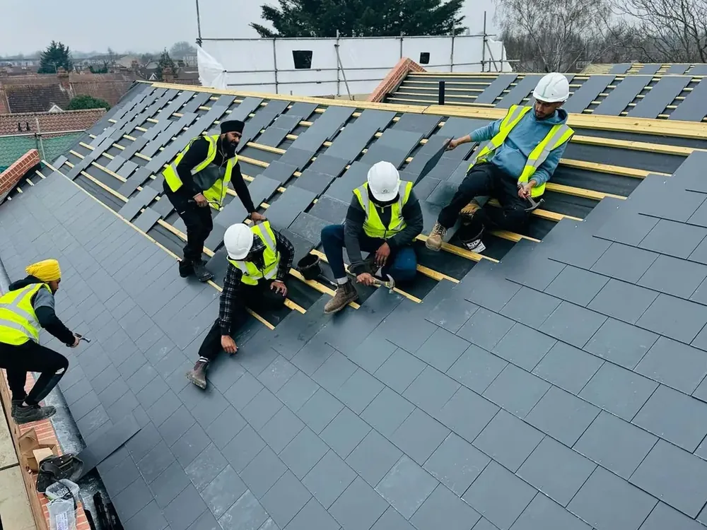 Roofers in hi-vis and hard hats laying slates across new battens