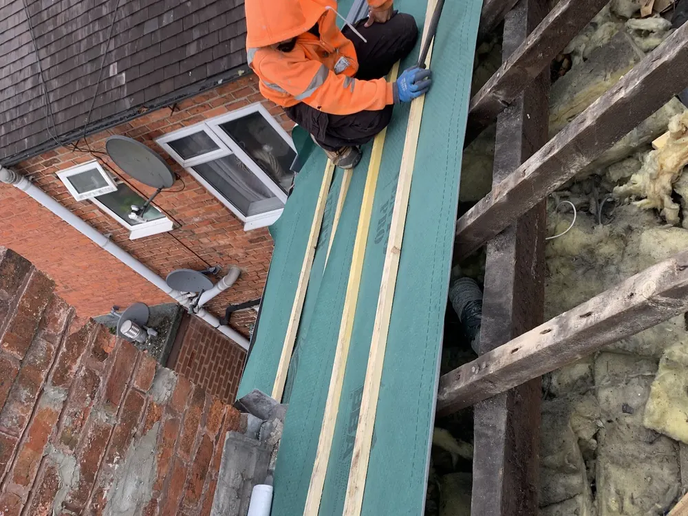 Roofer fixing battens over green membrane on a terrace roof