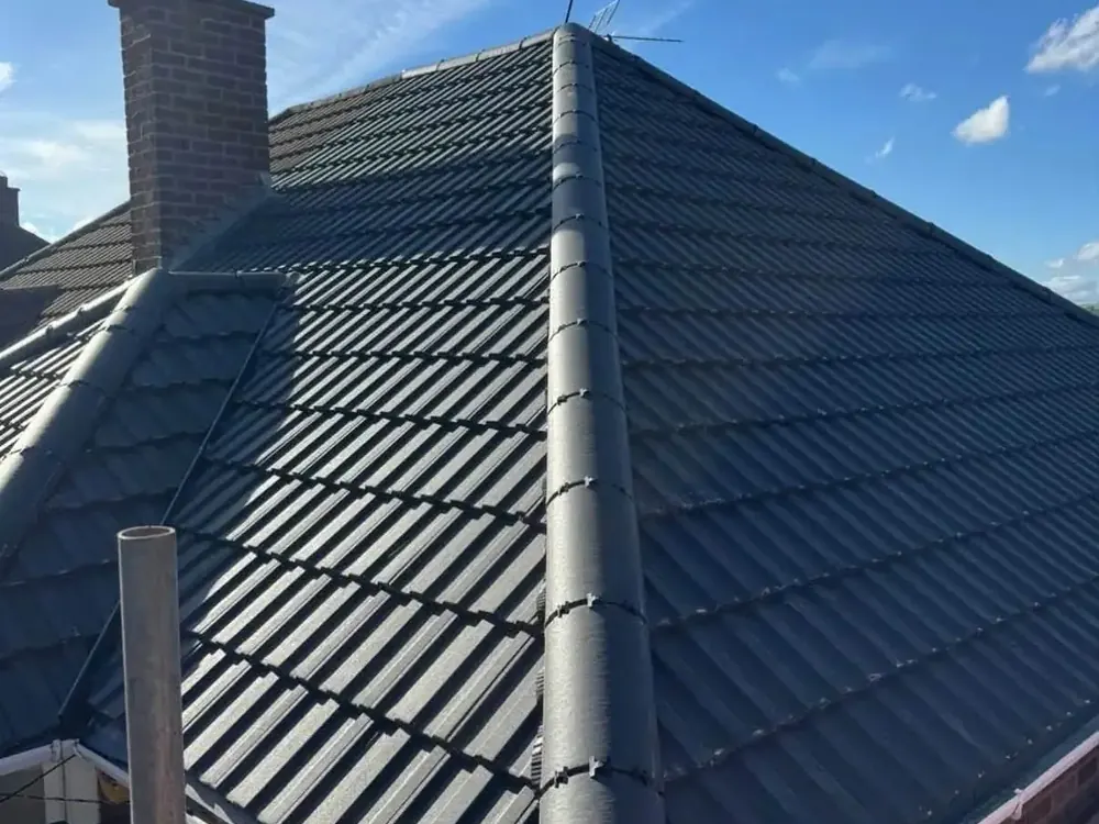 Finished grey tiled hip roof with a new ridge beside a brick chimney stack
